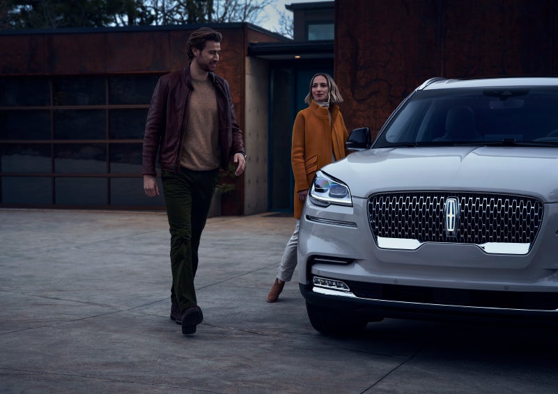 A man and a woman approaching a 2024 Lincoln Aviator® SUV, which illuminates certain lights when they are close | Lincoln Demo 2 in Wooster OH