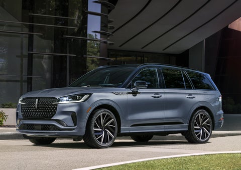A gray 2025 Lincoln Aviator® SUV is parked outside a modern building showcasing the driver’s side of the vehicle. | Lincoln Demo 2 in Wooster OH