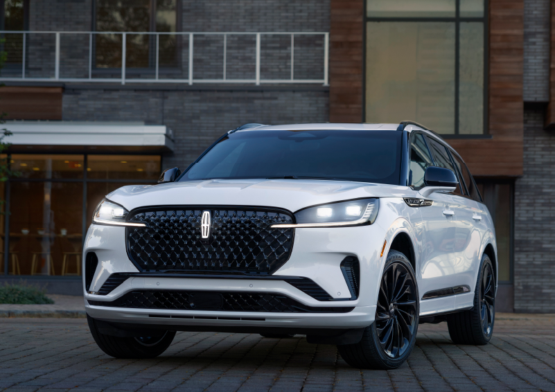 A white 2025 Lincoln Aviator® SUV is shown parked outside a modern building with gray brick and wood accents. | Lincoln Demo 2 in Wooster OH