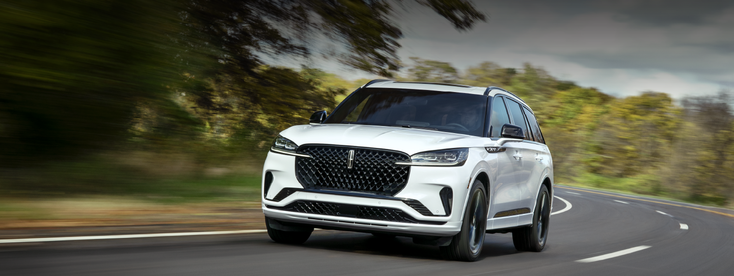 A white 2025 Lincoln Aviator® SUV is being driven down a road lined with trees. | Lincoln Demo 2 in Wooster OH